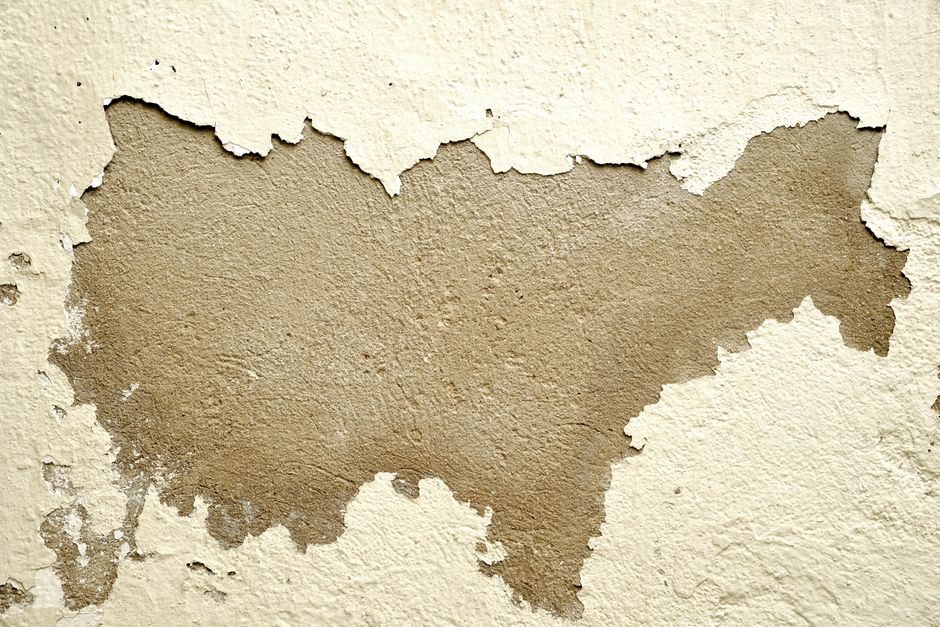 Close-up of a wall with peeling paint revealing the rough texture underneath.